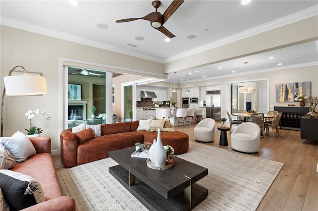 living area with light wood-type flooring, visible vents, ornamental molding, recessed lighting, and ceiling fan