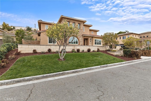 mediterranean / spanish house featuring stucco siding, stone siding, fence, a front yard, and a tiled roof