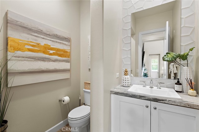 half bathroom with vanity, toilet, and baseboards