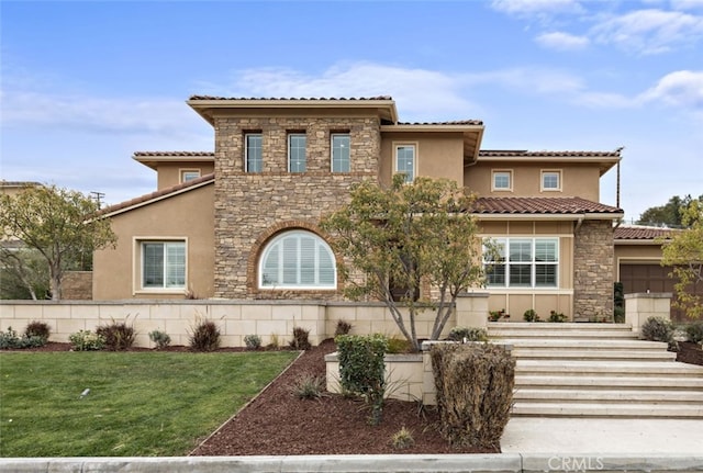 mediterranean / spanish-style home with stucco siding, stone siding, a front yard, and a tile roof