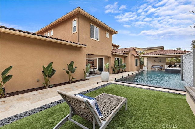 back of property with a patio area, stucco siding, an outdoor pool, and a lawn