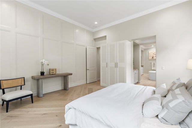 bedroom with recessed lighting, connected bathroom, a decorative wall, crown molding, and light wood finished floors