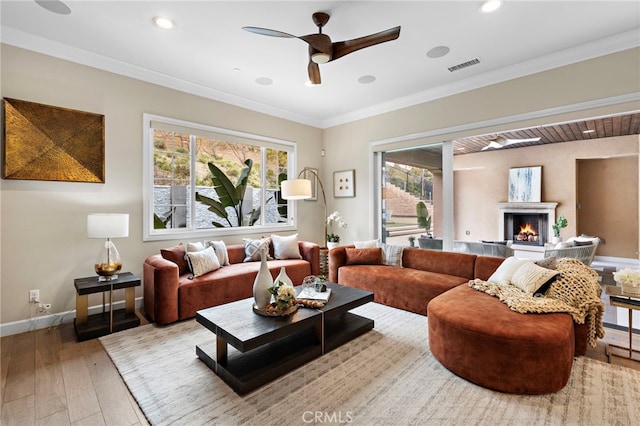 living room with visible vents, hardwood / wood-style floors, a lit fireplace, crown molding, and baseboards