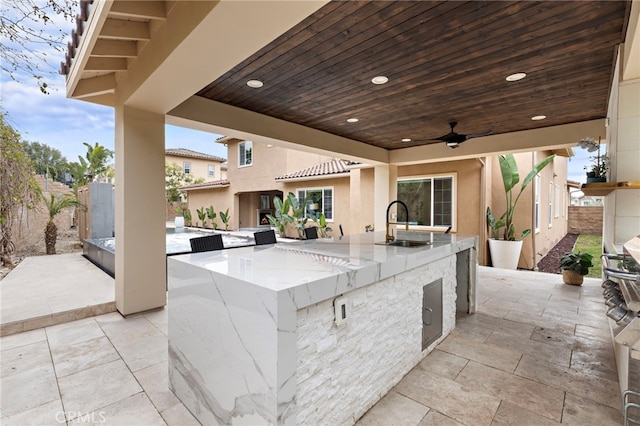 view of patio with fence, exterior kitchen, outdoor wet bar, ceiling fan, and a sink