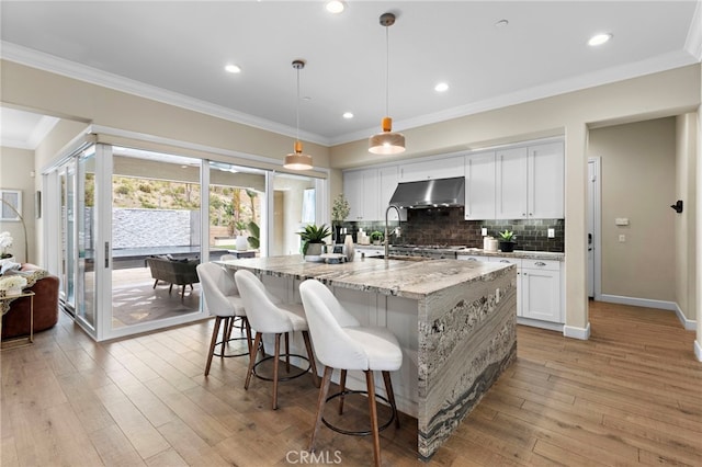 kitchen featuring range hood, ornamental molding, white cabinets, light wood-type flooring, and backsplash