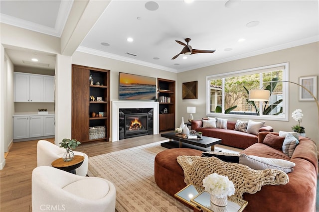 living area featuring visible vents, light wood-style flooring, recessed lighting, a fireplace, and crown molding