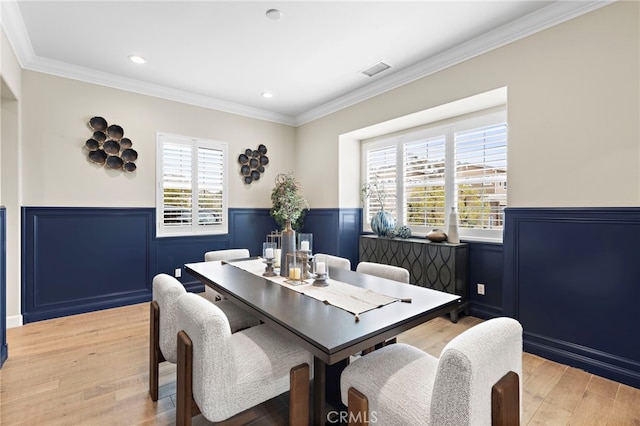 dining area featuring crown molding, light wood-type flooring, visible vents, and wainscoting