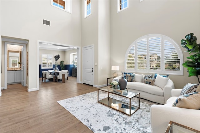 living room with visible vents, baseboards, ornamental molding, light wood-style flooring, and a towering ceiling