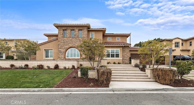 mediterranean / spanish home featuring stone siding, a garage, a front yard, and stucco siding