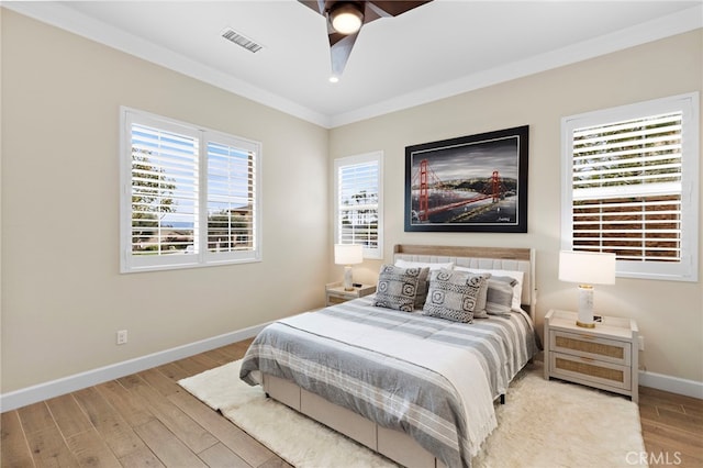 bedroom with wood finished floors, visible vents, baseboards, ceiling fan, and crown molding