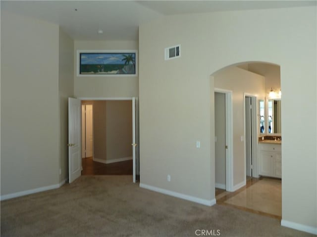 unfurnished bedroom featuring arched walkways, high vaulted ceiling, visible vents, baseboards, and carpet