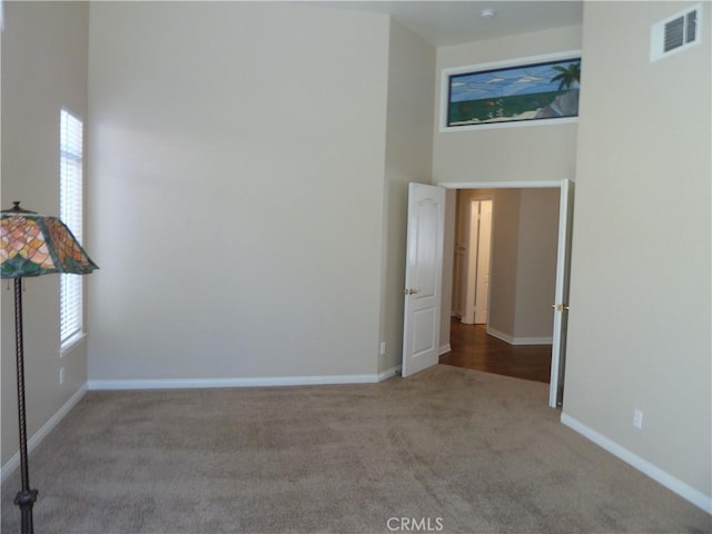 carpeted empty room with a healthy amount of sunlight, visible vents, baseboards, and a high ceiling