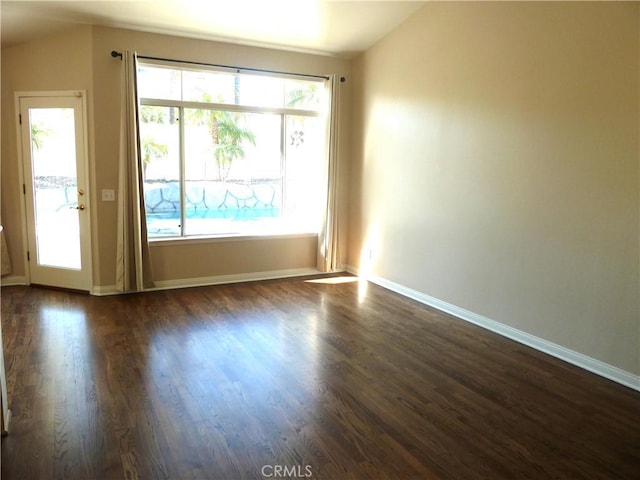 spare room with vaulted ceiling, dark wood-style floors, and baseboards