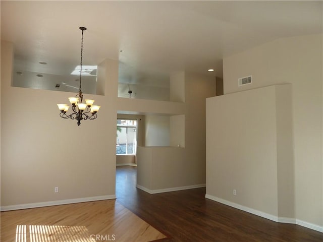 empty room with visible vents, a notable chandelier, baseboards, and wood finished floors