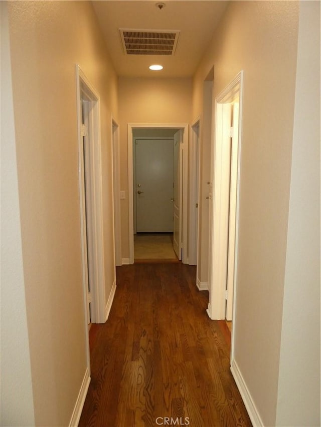 hall with baseboards, visible vents, and dark wood-type flooring