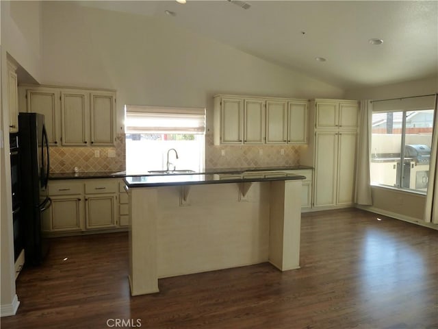 kitchen with cream cabinetry, dark wood finished floors, lofted ceiling, dark countertops, and a sink