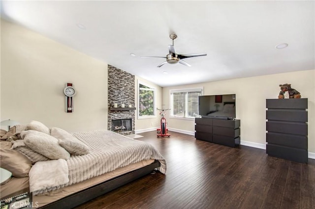 bedroom featuring baseboards, a stone fireplace, wood finished floors, and a ceiling fan