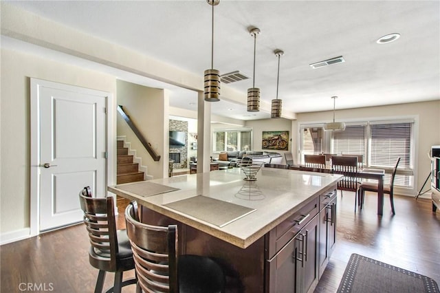 kitchen featuring visible vents, pendant lighting, a center island, dark brown cabinetry, and dark wood-style flooring