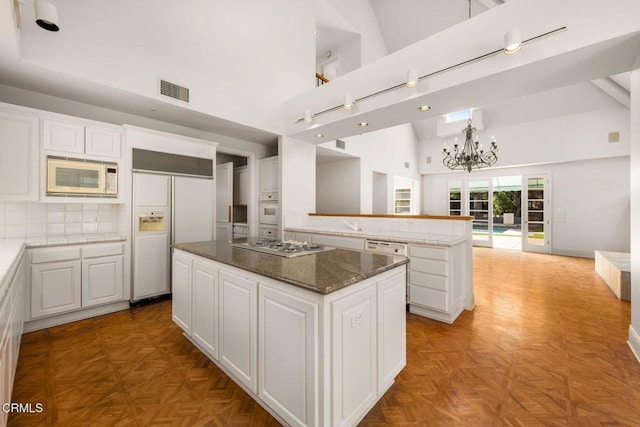 kitchen with white appliances, visible vents, white cabinets, a center island, and high vaulted ceiling