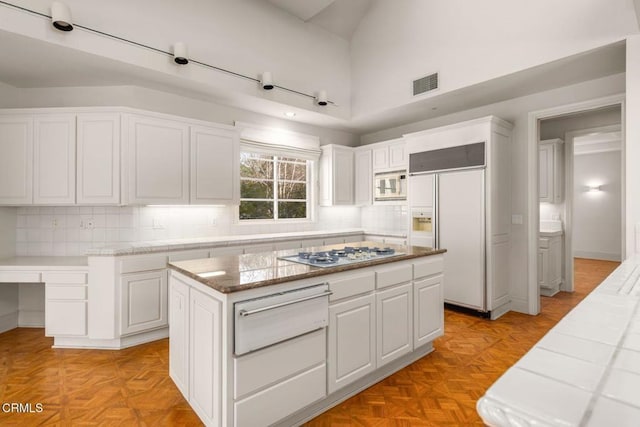 kitchen with visible vents, white cabinets, built in appliances, backsplash, and a warming drawer