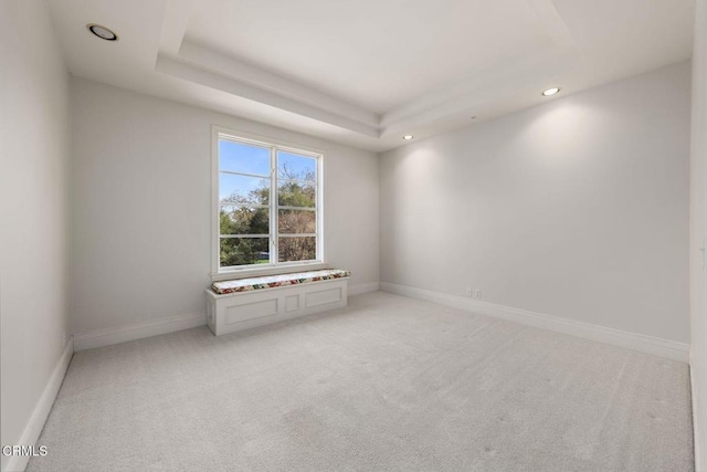 empty room featuring light carpet, recessed lighting, a raised ceiling, and baseboards