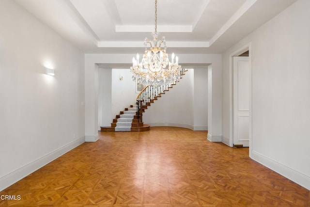 empty room featuring stairway, baseboards, a raised ceiling, and a notable chandelier