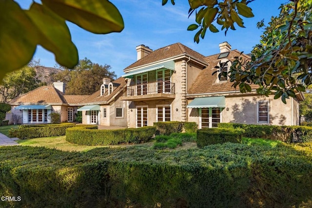 back of property with a lawn, a chimney, a balcony, and stucco siding