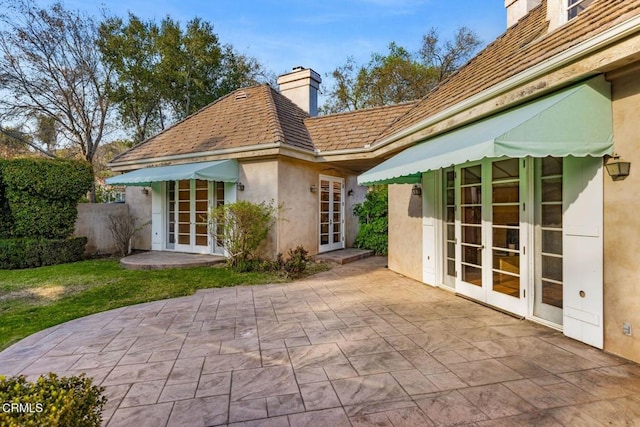 rear view of property featuring french doors, a patio area, a chimney, and stucco siding