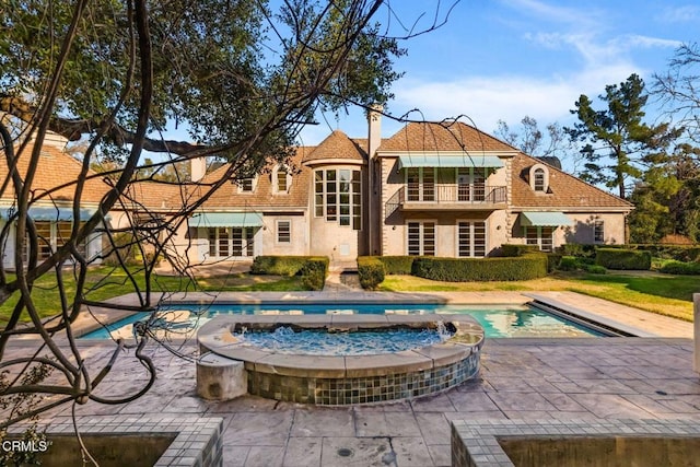 back of house featuring stucco siding, a pool with connected hot tub, a chimney, and a patio