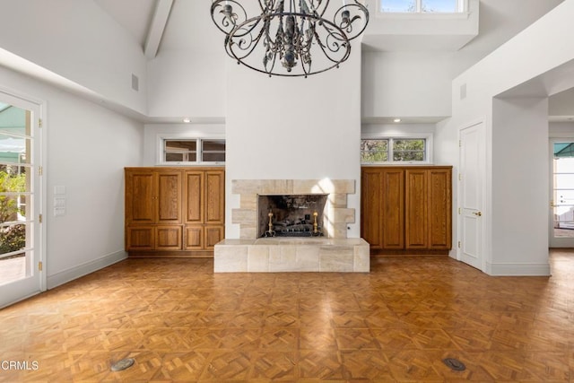 unfurnished living room with baseboards, a fireplace with raised hearth, a high ceiling, and a healthy amount of sunlight