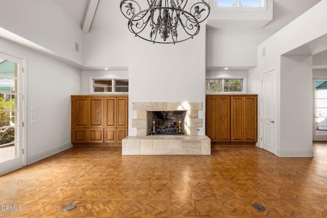 unfurnished living room featuring baseboards, high vaulted ceiling, beamed ceiling, and a healthy amount of sunlight