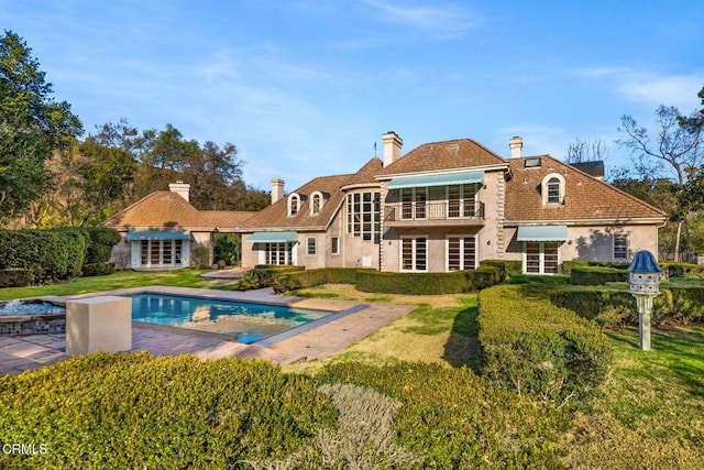 back of house featuring stucco siding, a chimney, an outdoor pool, and a yard