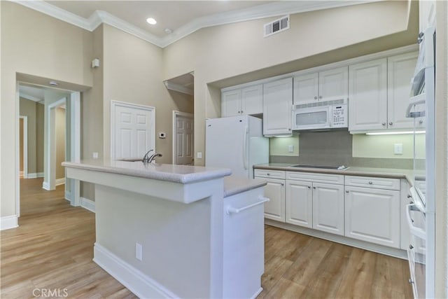 kitchen with white appliances, visible vents, light wood-style floors, white cabinetry, and a center island with sink