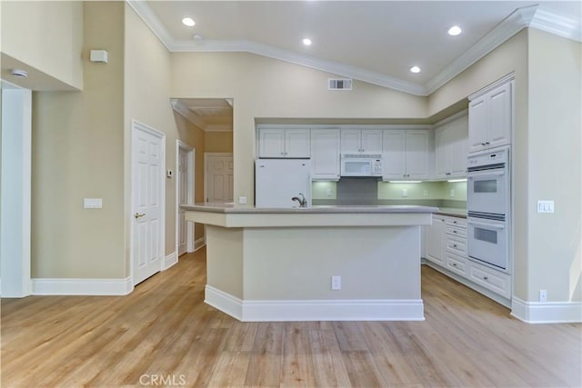 kitchen with crown molding, light wood finished floors, visible vents, an island with sink, and white appliances