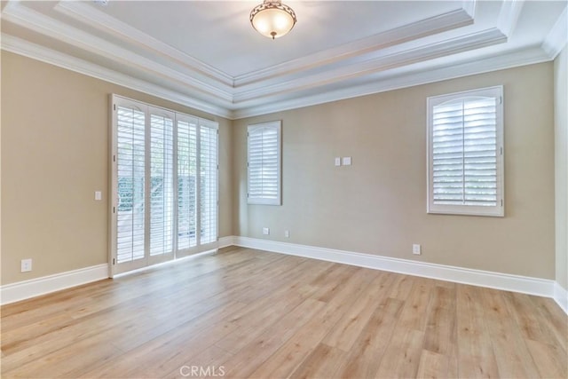 unfurnished room with light wood-type flooring, a raised ceiling, crown molding, and baseboards