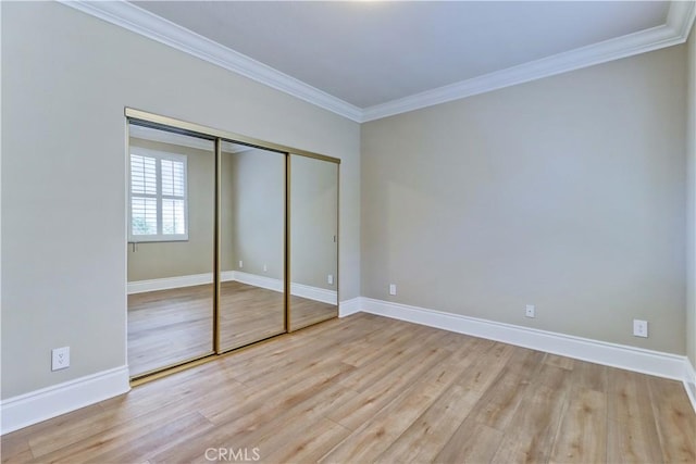 unfurnished bedroom featuring baseboards, a closet, wood finished floors, and crown molding