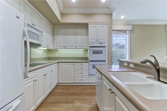 kitchen featuring white appliances, a sink, white cabinets, ornamental molding, and light wood-type flooring