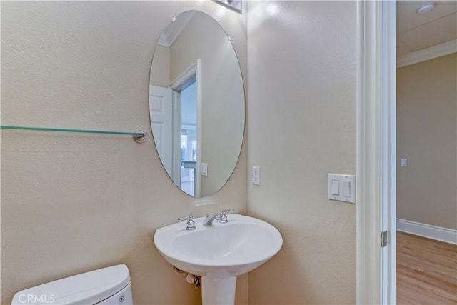 half bath featuring baseboards, a sink, toilet, and wood finished floors