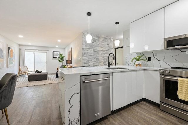 kitchen with a peninsula, a sink, white cabinets, appliances with stainless steel finishes, and decorative backsplash