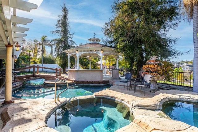 view of pool with fence, outdoor dry bar, a gazebo, and an in ground hot tub