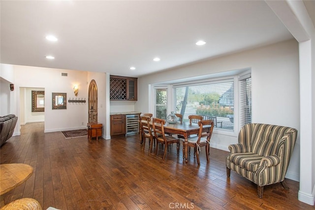 dining space with dark wood-type flooring, beverage cooler, baseboards, and a dry bar