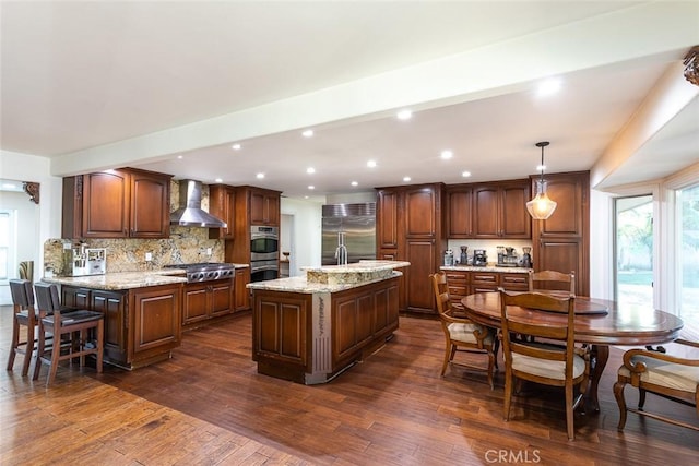 kitchen with stainless steel appliances, wall chimney range hood, dark wood-type flooring, and decorative backsplash