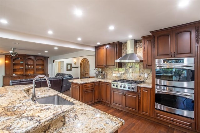 kitchen featuring dark wood-style floors, wall chimney exhaust hood, appliances with stainless steel finishes, a sink, and backsplash