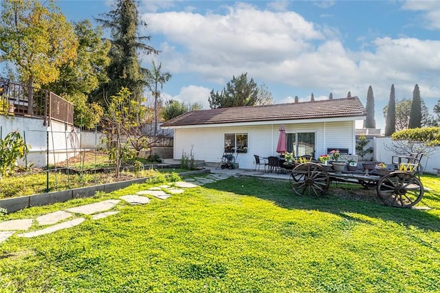 rear view of house featuring a patio, a lawn, fence private yard, and a vegetable garden