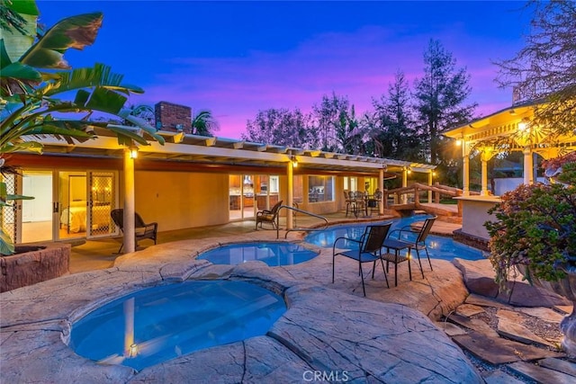 pool at dusk with a patio area and a pool with connected hot tub