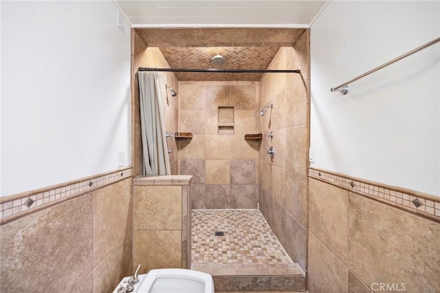 bathroom featuring wainscoting, tiled shower, and tile walls