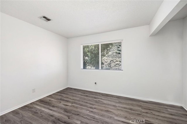 spare room with dark wood-style floors, baseboards, visible vents, and a textured ceiling