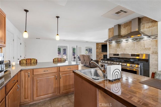 kitchen with visible vents, a peninsula, wall chimney range hood, a sink, and gas stove