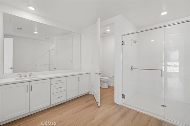 bathroom featuring a stall shower, toilet, wood finished floors, vanity, and recessed lighting