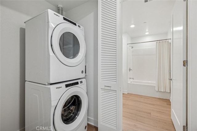 clothes washing area featuring laundry area, stacked washer and clothes dryer, and light wood-style floors